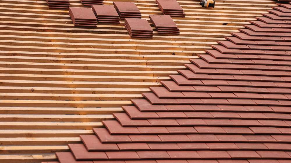 Couvreur posant des tuiles en terre cuite sur une toiture en rénovation en Provence
